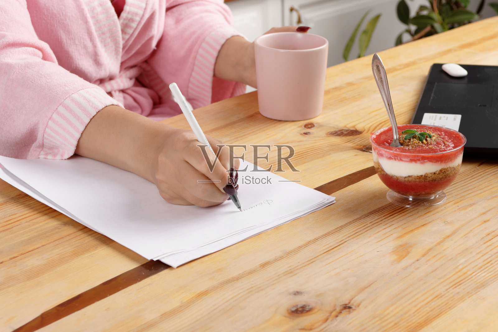 淋浴后穿着浴袍的女人在家庭办公室吃美味的甜点作为早餐。照片摄影图片