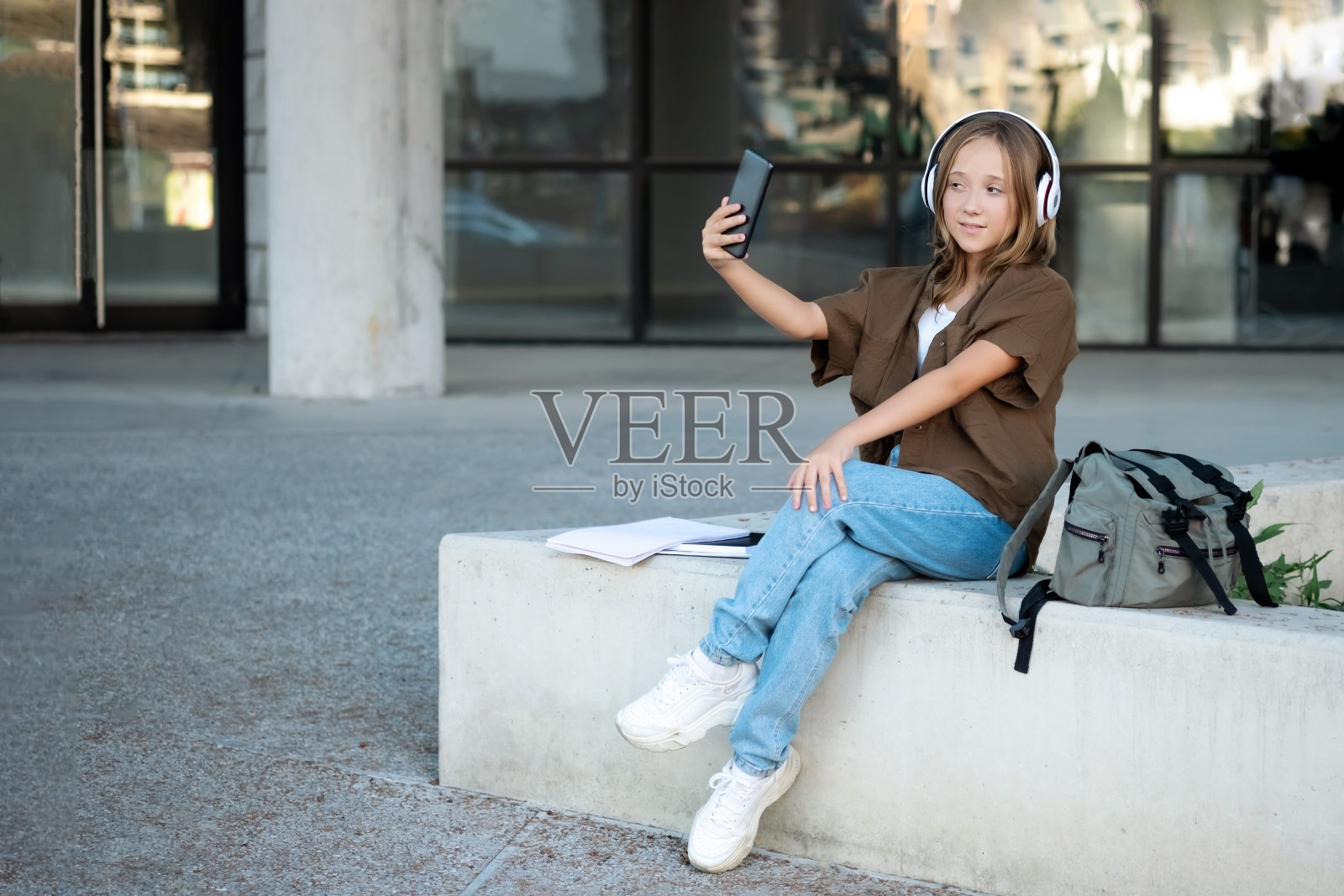 年轻的少女在城市街头,耳机听音乐,自拍,牛仔裤,背包,积极,春季潮流,城市青少年风格照片摄影图片