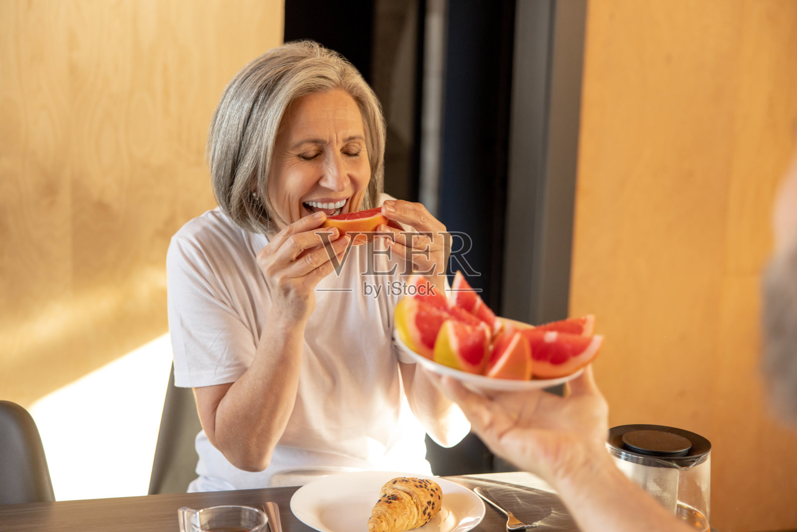 白发微笑的女人早餐吃葡萄柚照片摄影图片