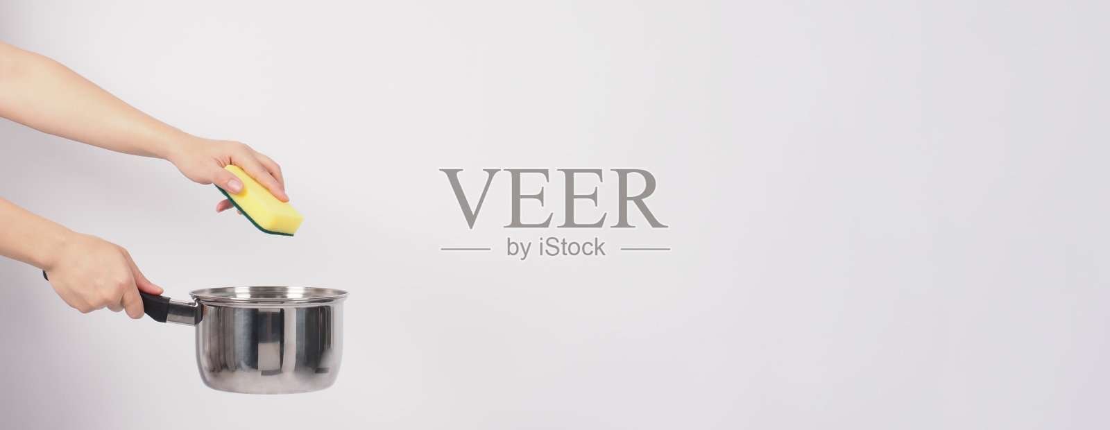 清洁锅的人在白色的背景上用方便的洗碗海绵清洁不粘锅,软的一面是黄色,硬的一面是绿色,以保证烹饪后的卫生。电锅照片摄影图片