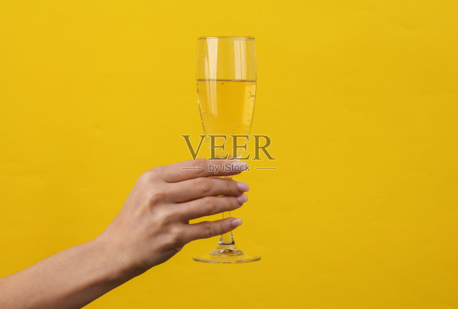 女人的手拿着黄色背景的香槟酒杯。有创意的想法。”照片摄影图片
