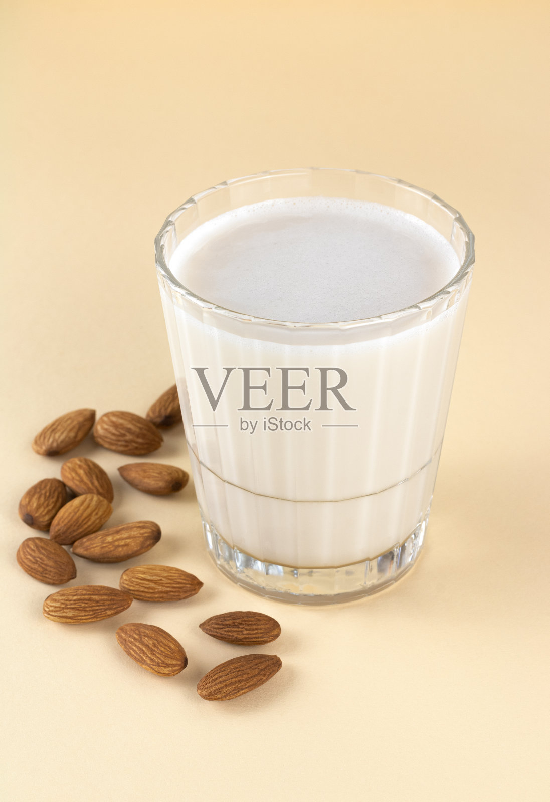 米色背景的玻璃杯里的杏仁奶和杏仁仁。不含乳糖的坚果牛奶。照片摄影图片