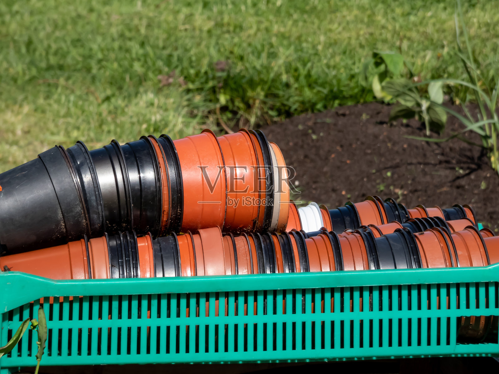 大的绿色塑料盒装满了棕色和黑色的塑料花盆,在阳光明媚的日子里,背景是花坛。园艺的概念照片摄影图片