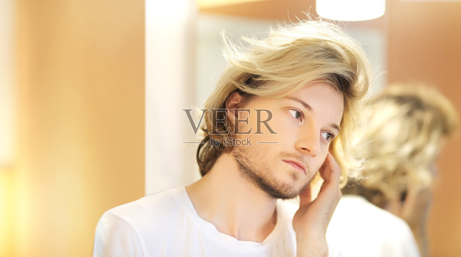 年轻人看着镜子,梳着头发,把问题放在脸上。照片摄影图片