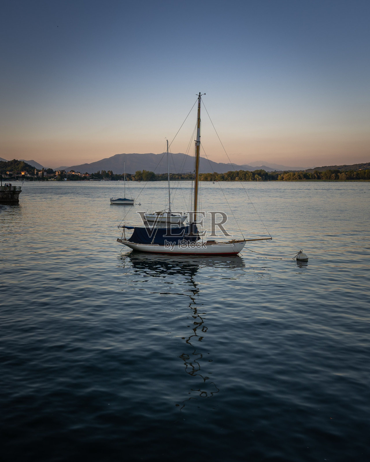 垂直拍摄一艘船停泊在港口对绿色海岸和山脉日落在意大利照片摄影图片