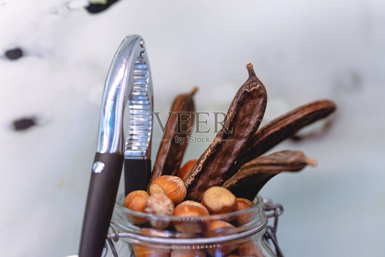 一个装满榛子和角豆的透明罐子的特写,还有一个胡桃夹子照片摄影图片
