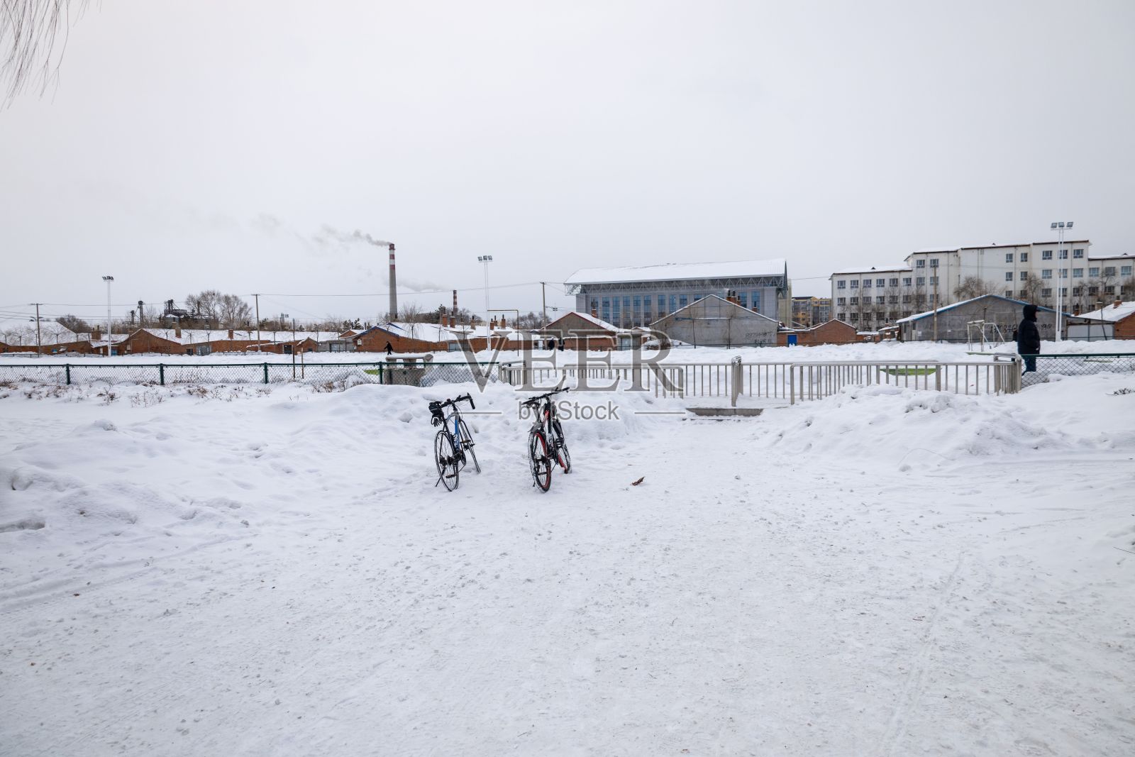 两辆自行车停在白雪覆盖的院子里,背景是公寓楼照片摄影图片