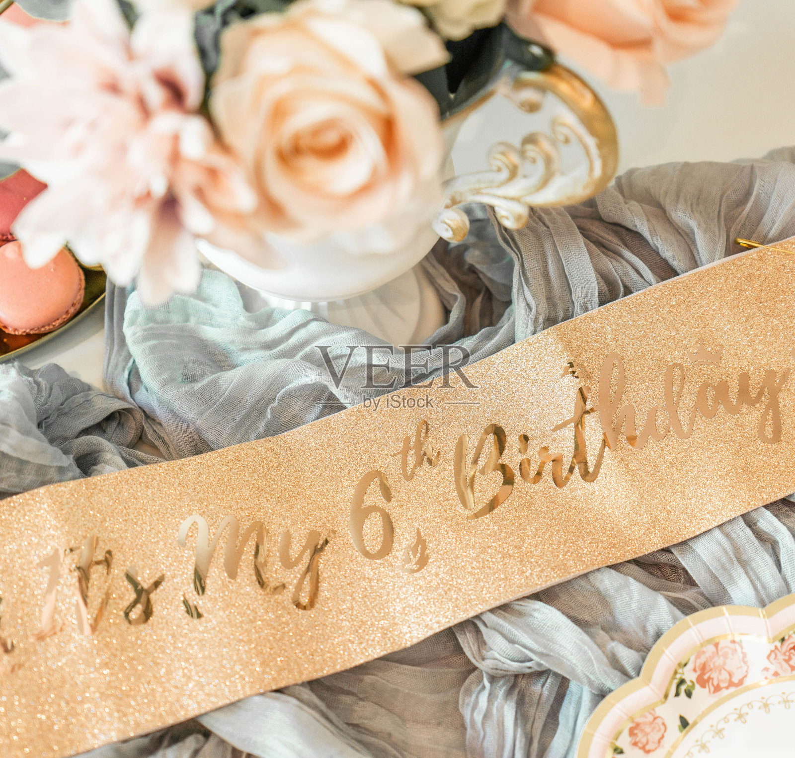 顶部特写的金色闪闪发光的生日绶带,上面写着“这是我的6岁生日”,旁边有一些花照片摄影图片