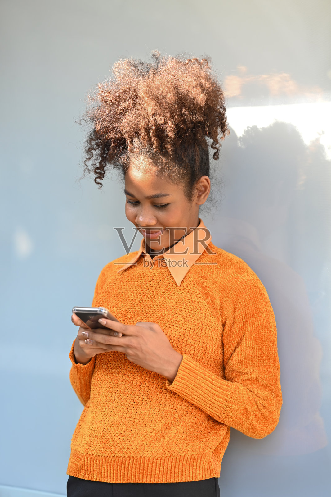 微笑的美国非洲妇女使用手机,站在办公大楼附近的户外。照片摄影图片