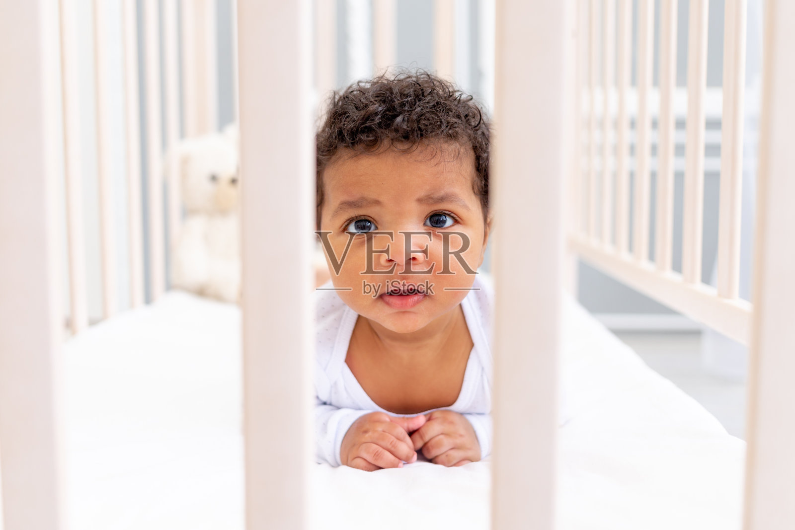 可爱的非裔美国小婴儿在白色的床上睡觉,看着旁边照片摄影图片