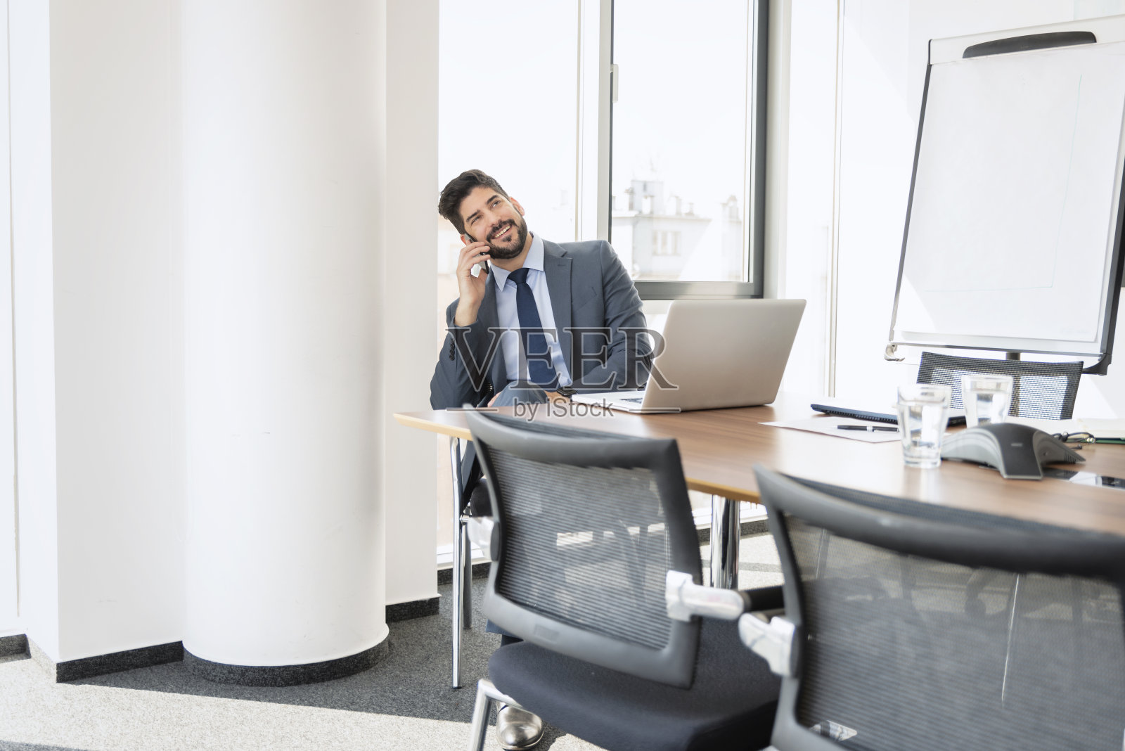 在一间现代化的办公室里,一位高级商人坐在他的笔记本电脑后面打商务电话照片摄影图片