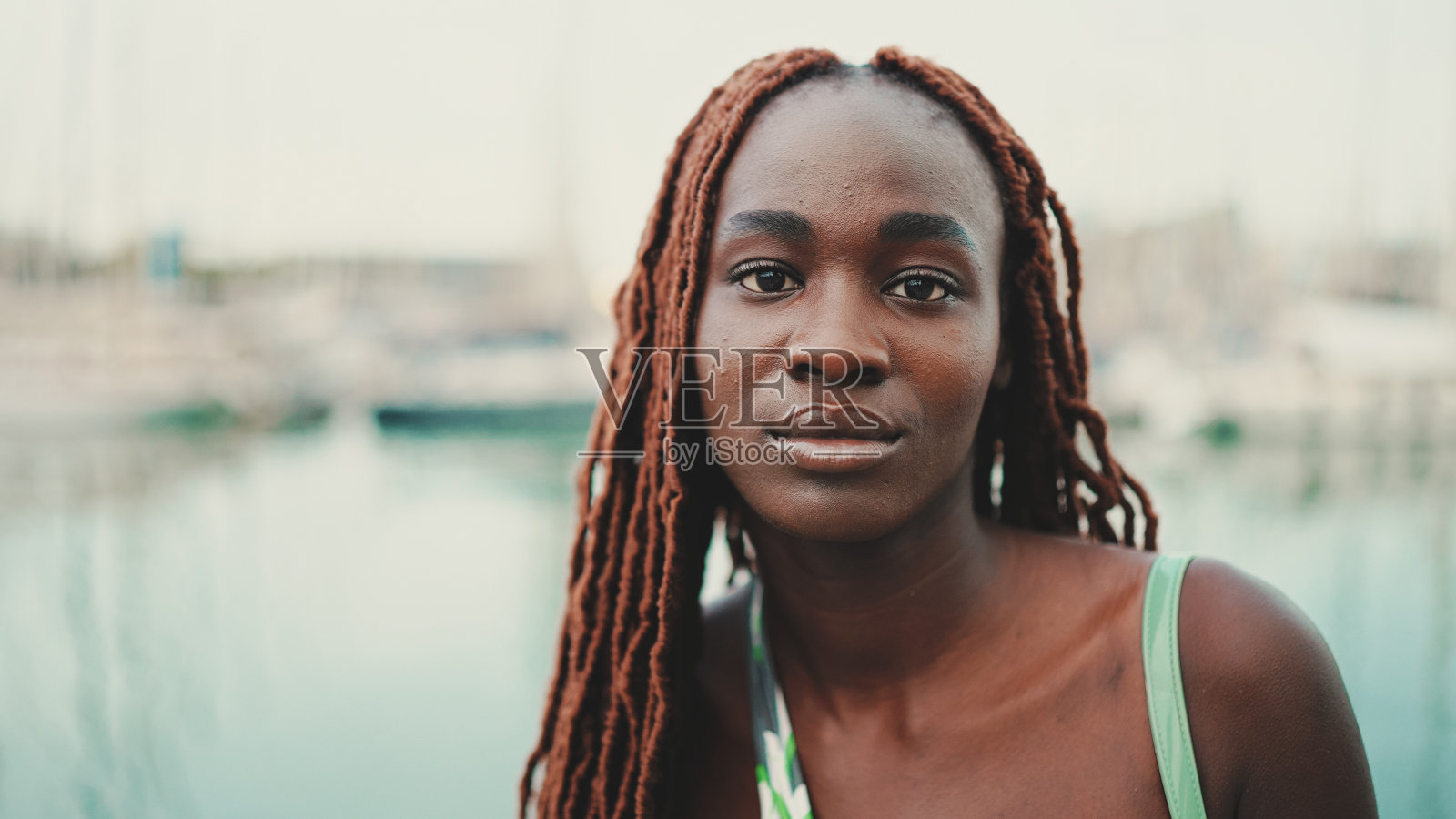 一名梳着非洲辫子、穿着上衣的女子看着码头上的游艇和船只。照片摄影图片