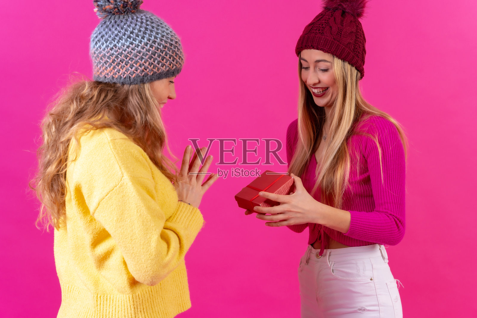 两个年轻的金发白人女子微笑着看着粉红色背景上的女朋友送的礼物照片摄影图片