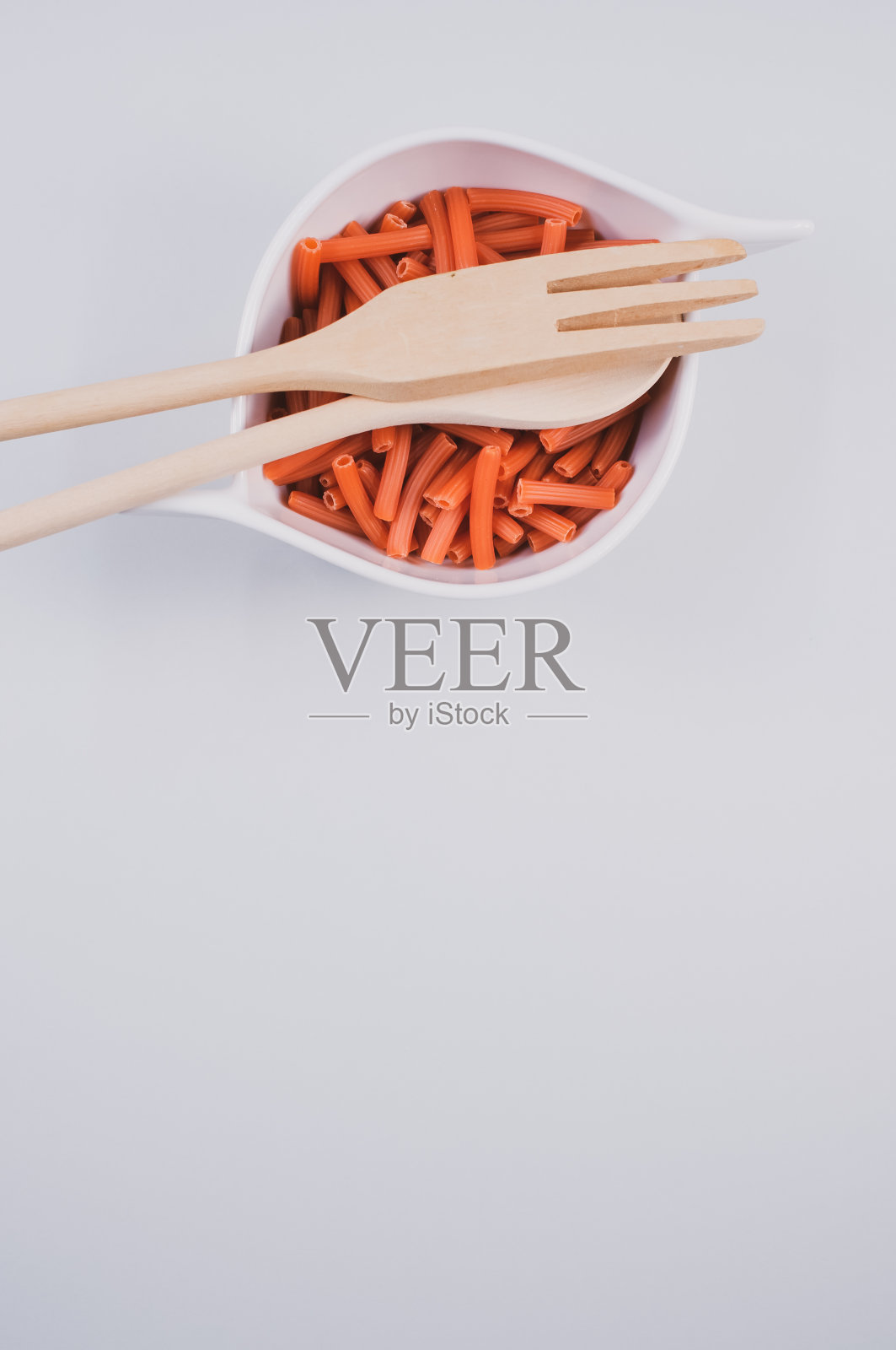 一碗干通心粉,木勺和叉子分开放在白色背景上照片摄影图片