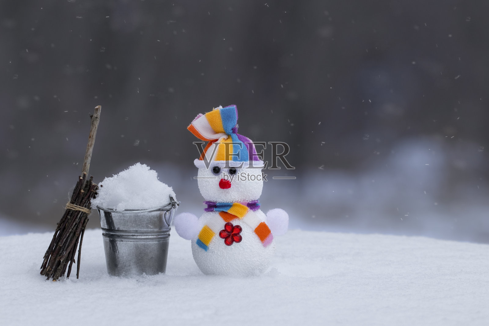 雪地里的玩具雪人。有趣的雪人与桶和扫帚上的天然雪。冬天的主题。照片摄影图片