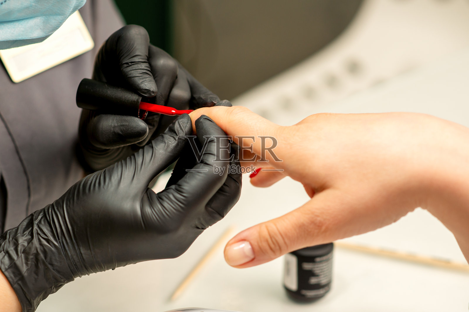 美甲清漆。在美容院,一名美甲师戴着黑色橡胶手套,正在给一名女性指甲涂上红色清漆。照片摄影图片