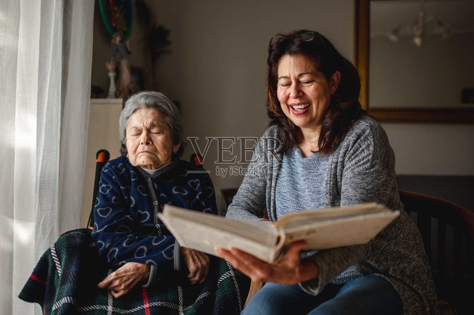 微笑的女儿拿着一本相册,旁边是坐在轮椅上生病的母亲照片摄影图片