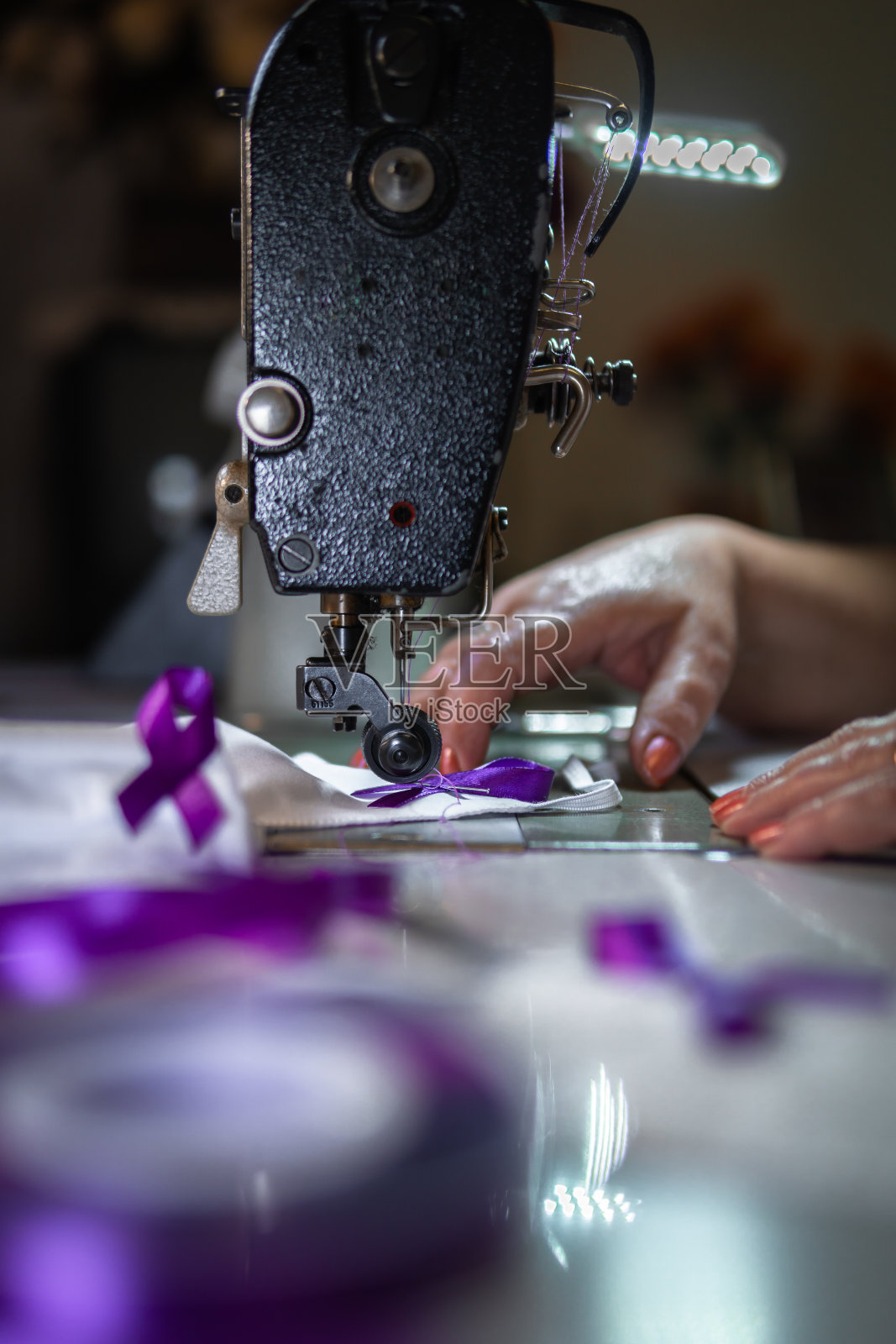 垂直拍摄车间里一个人在口罩上缝紫色丝带——COVID-19意识照片摄影图片