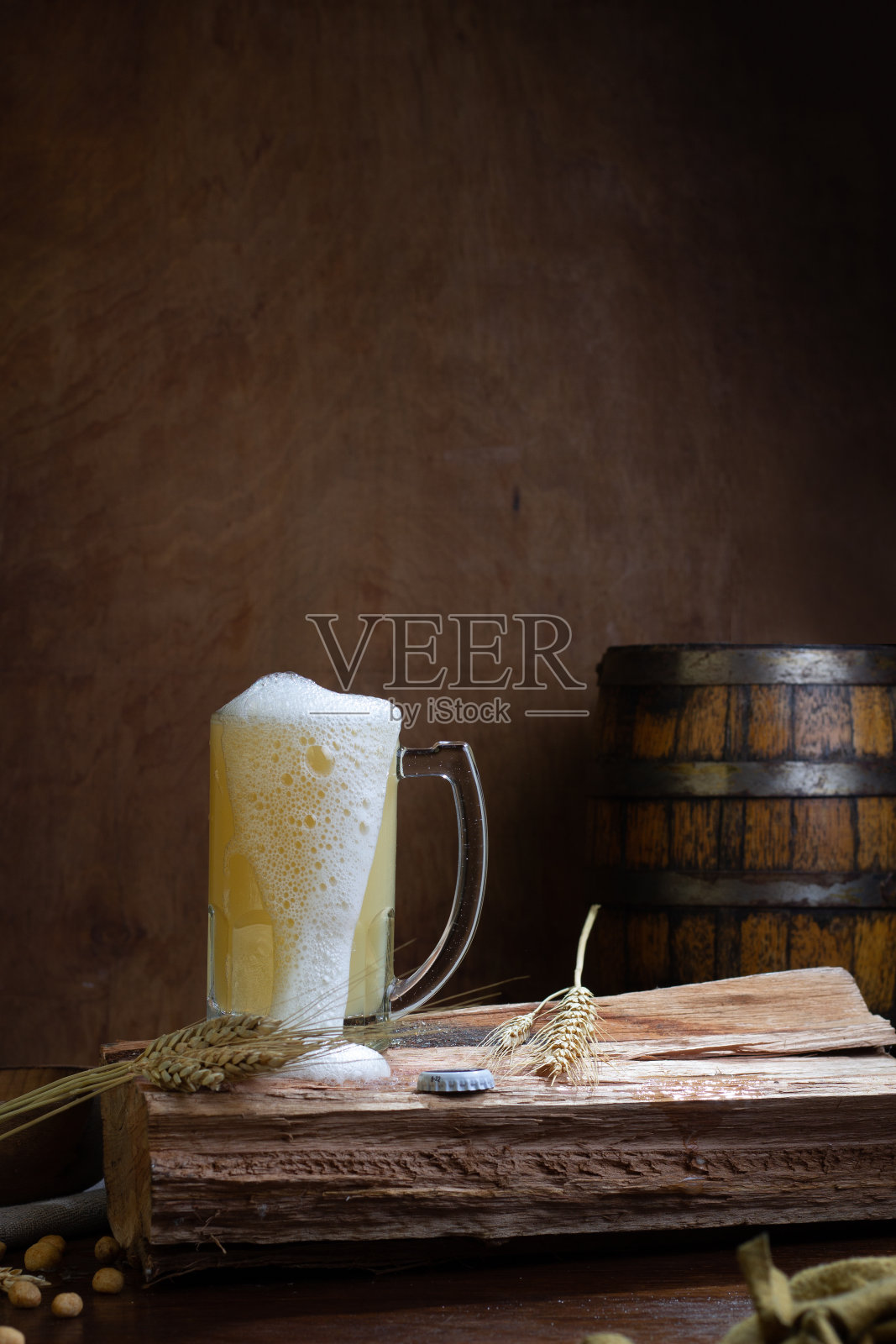 垂直镜头:木桌上的玻璃杯里盛着精酿啤酒,背景是一个木桶照片摄影图片