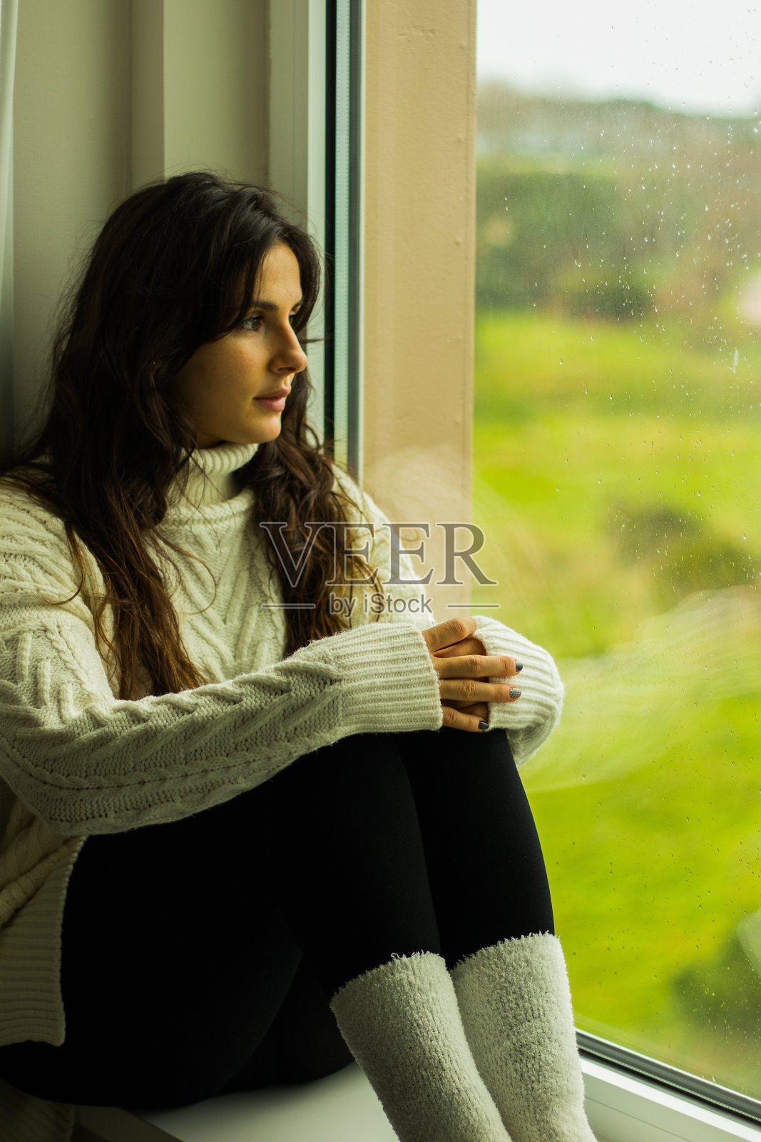 一个白人女性坐在窗台上,看着窗外的垂直镜头照片摄影图片