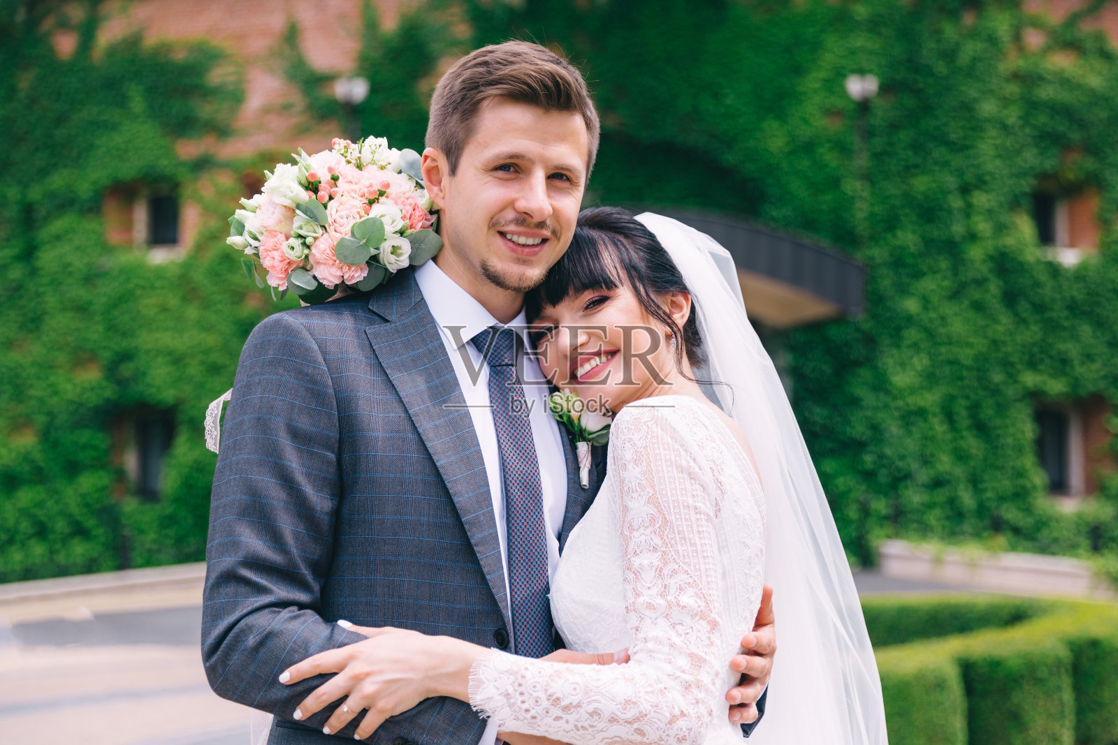 在街道上的老建筑附近,新郎穿着结婚礼服,新娘穿着礼服,手捧花束。新婚夫妇拥抱。照片摄影图片