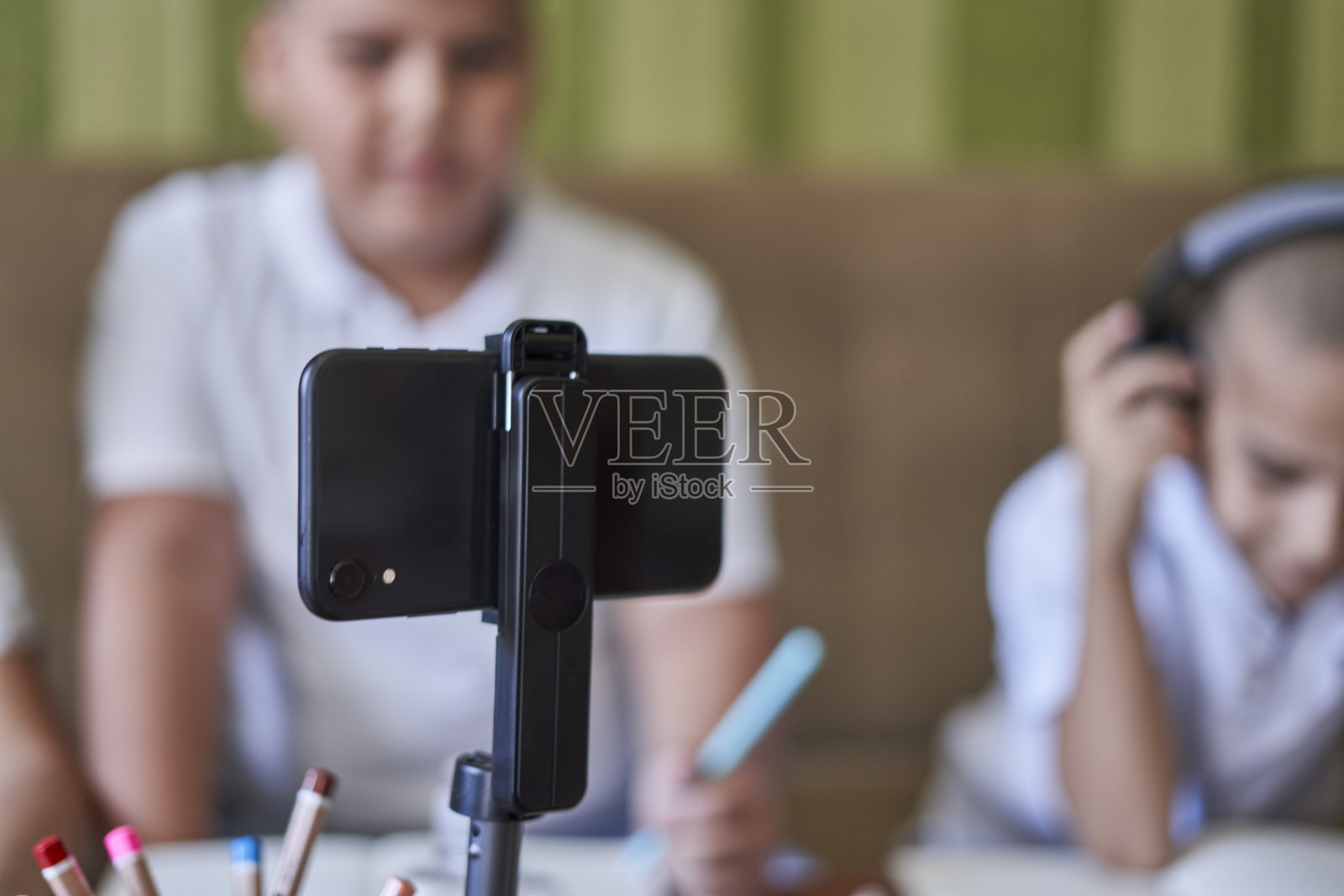 桌子上的架子上放着手机,背景是学生们正在听在线课程照片摄影图片