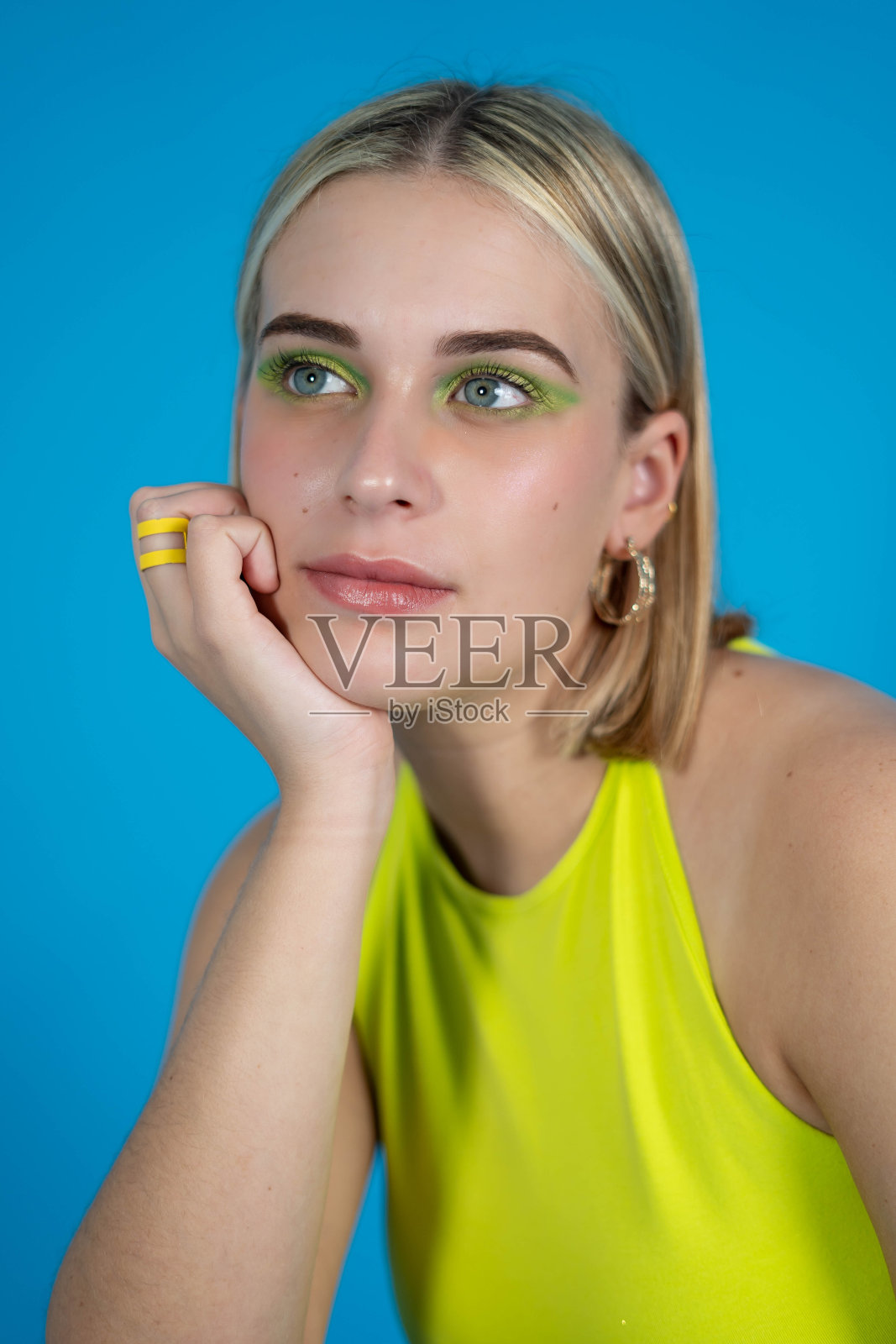一个年轻的西班牙女孩的肖像与绿色闪亮的眼影对蓝色背景摆姿势照片摄影图片