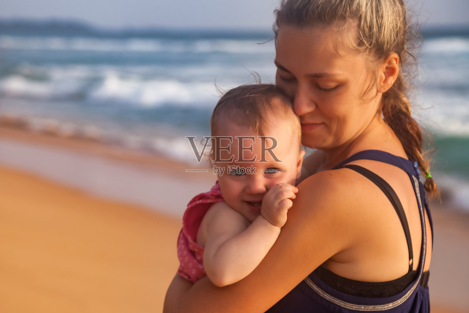 快乐的年轻妈妈抱着婴儿在热带沙滩在海上背景。女性带着小孩在暑假旅行。母亲的概念和与孩子的娱乐。复制文本空格照片摄影图片