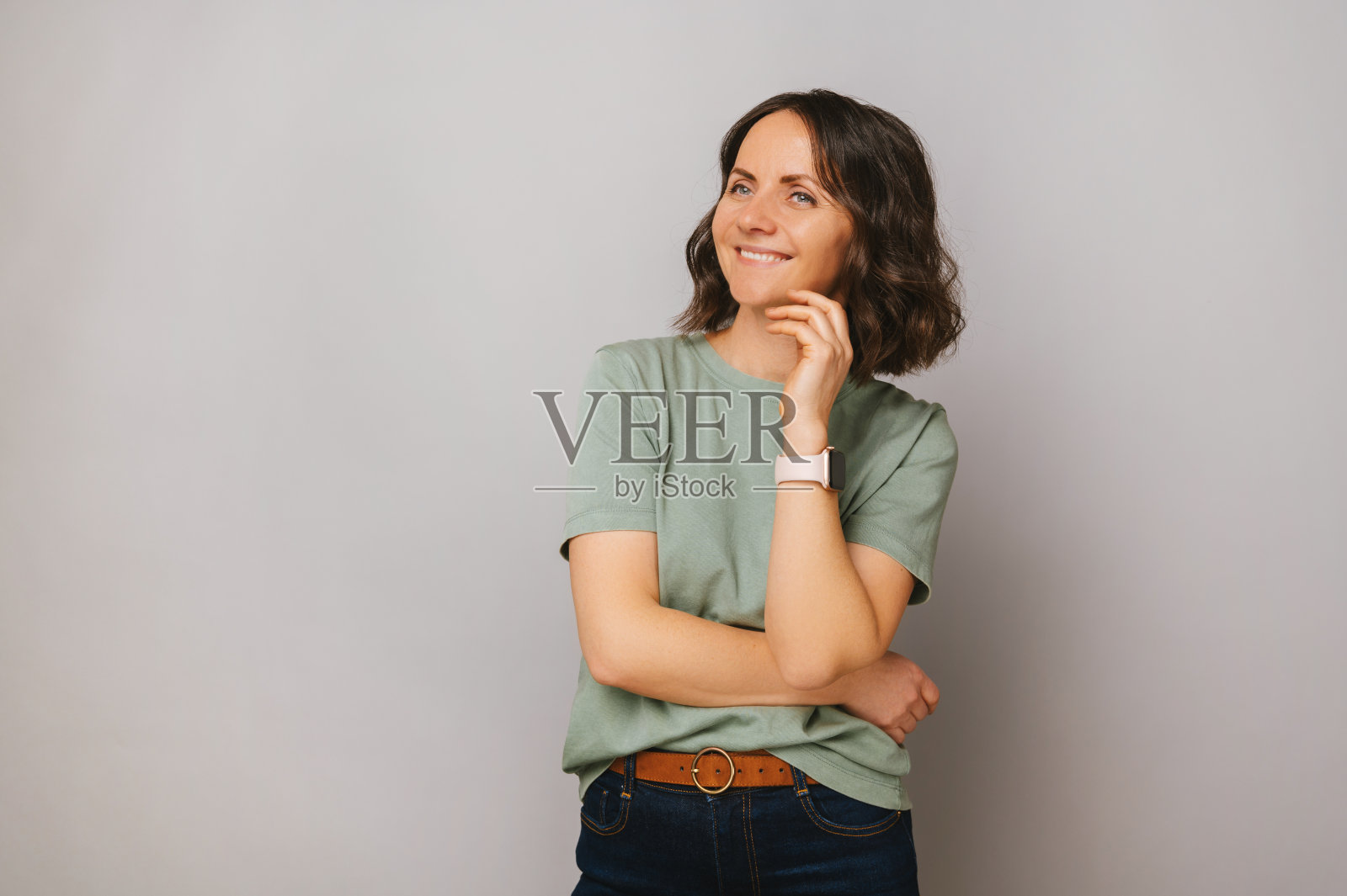 开朗的年轻女子穿着绿色t恤,手握在她的下巴下。照片摄影图片