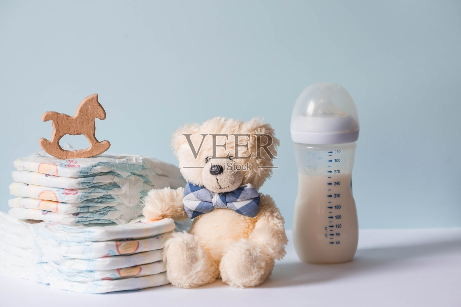 木制玩具,一只戴领结的熊,一堆尿布,一个奶瓶和婴儿用品放在换尿布的桌子上。文本空格。照片摄影图片