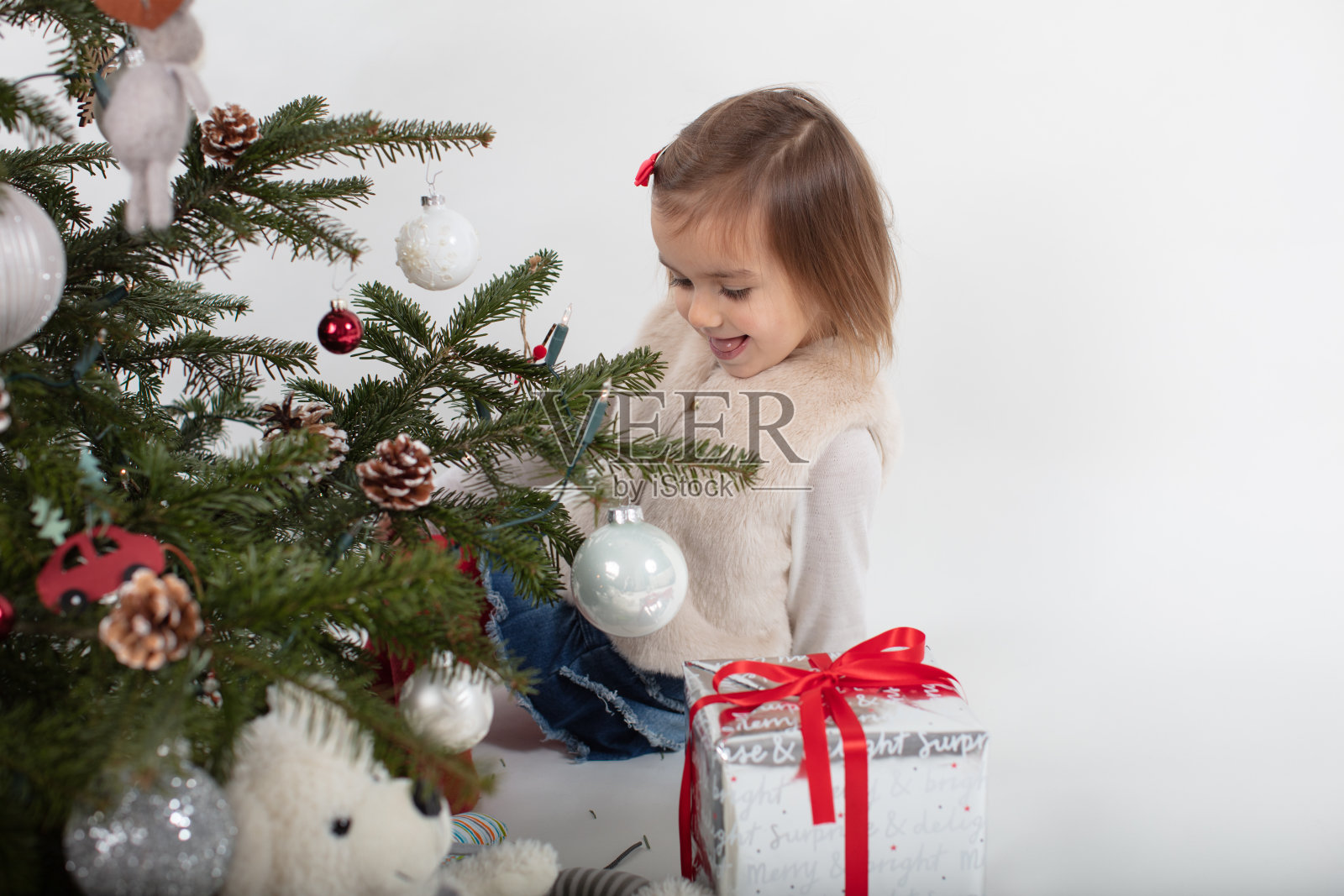 蹒跚学步的女孩兴高采烈地在圣诞树后玩耍照片摄影图片