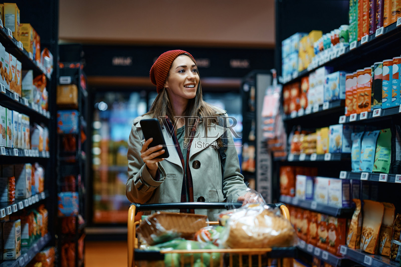 快乐的女人用手机在杂货店购物。照片摄影图片