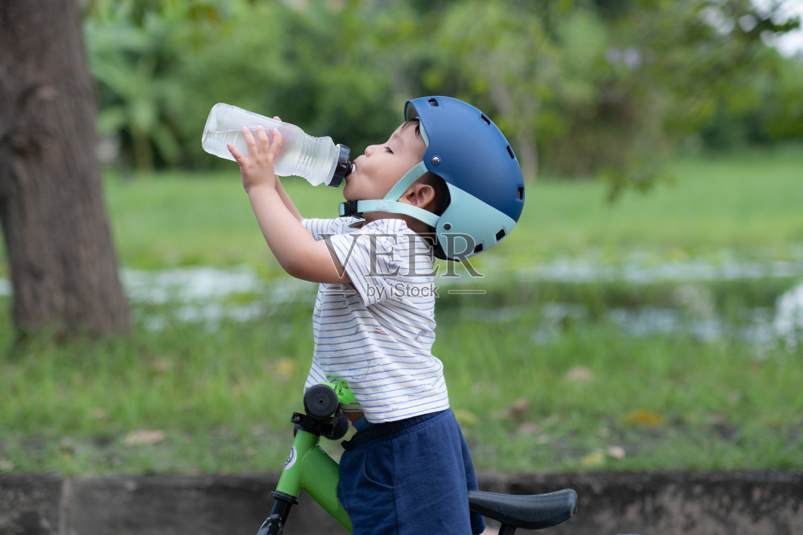 可爱的小男孩骑着自行车,戴着头盔,从水瓶里喝水照片摄影图片