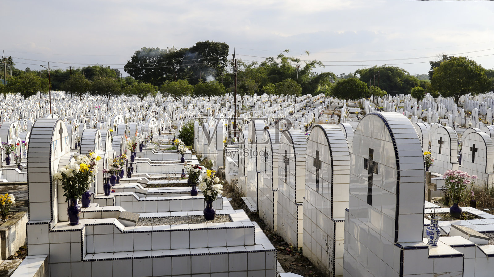 公共墓地有相同的白色陶瓷坟墓,上面有鲜花。照片摄影图片