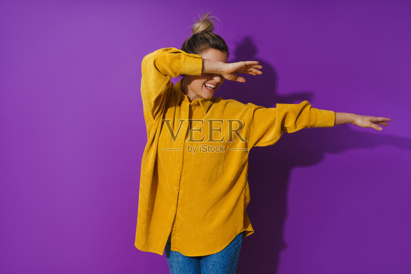 年轻开朗的女孩穿着黄色衬衫在紫色的背景跳舞照片摄影图片