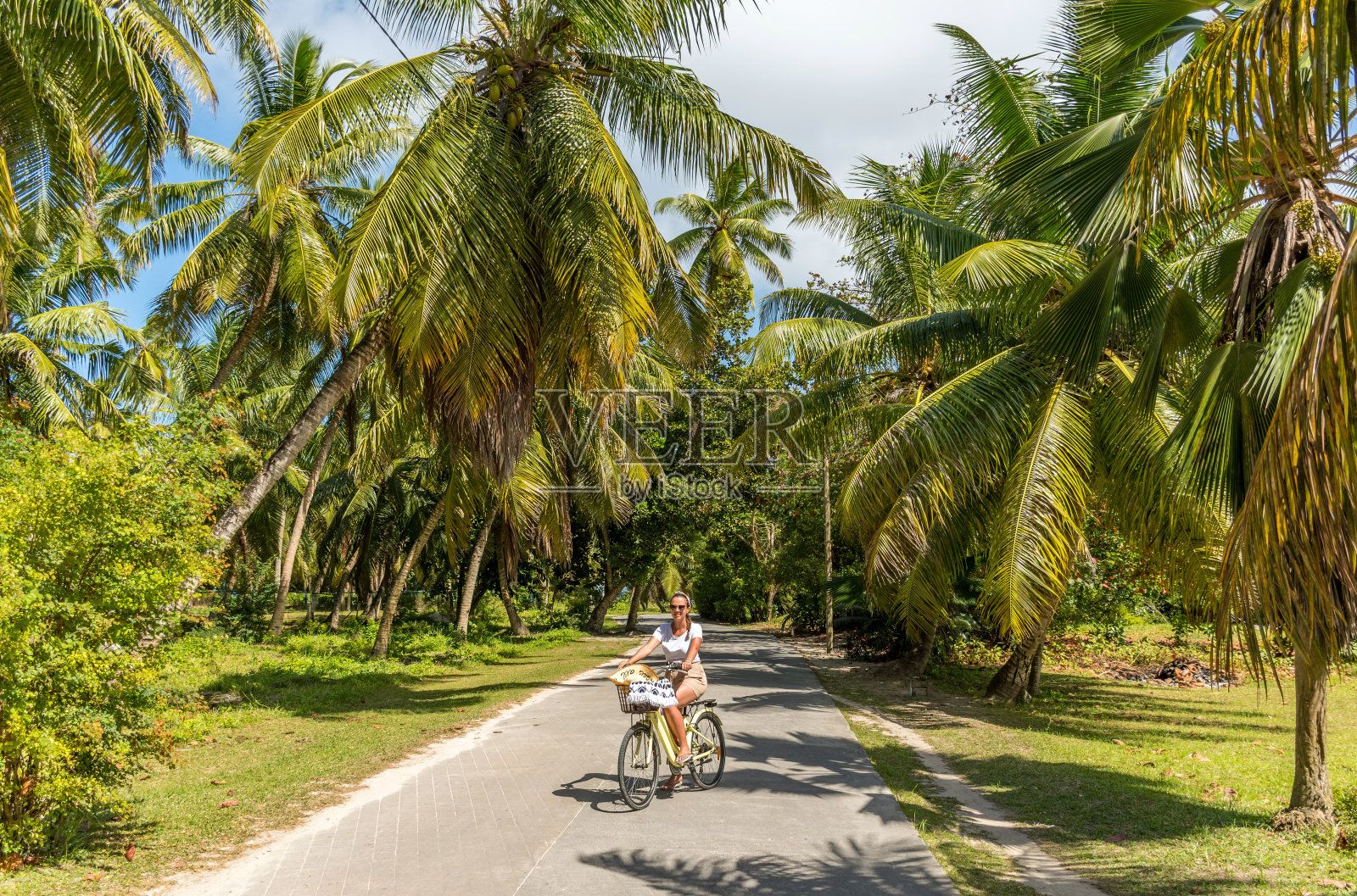 一个阳光明媚的日子,一个快乐的女人在热带花园骑自行车照片摄影图片