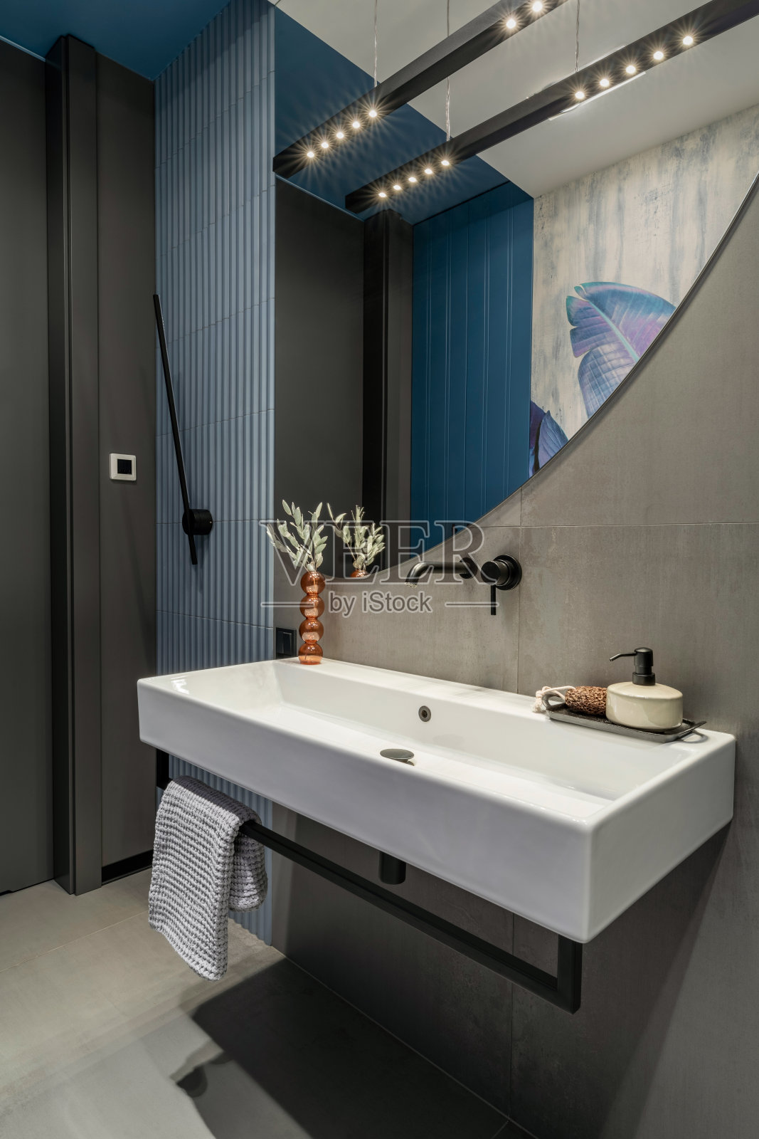 浴室内部设计:大镜子,白色丝绸,毛巾,灰色瓷砖,现代灯具,干花花瓶和个人配件。家居装饰。模板。照片摄影图片