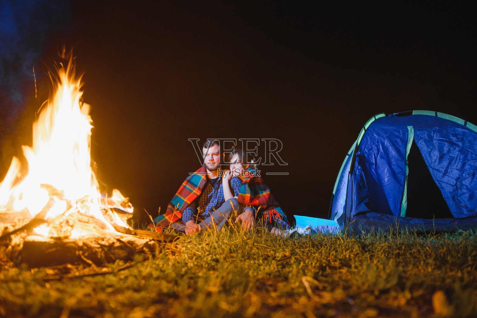 年轻夫妇在帐篷和蓝色游客帐篷旁的篝火旁休息,喝茶,欣赏夜空。带着帐篷积极娱乐和旅行的概念照片摄影图片