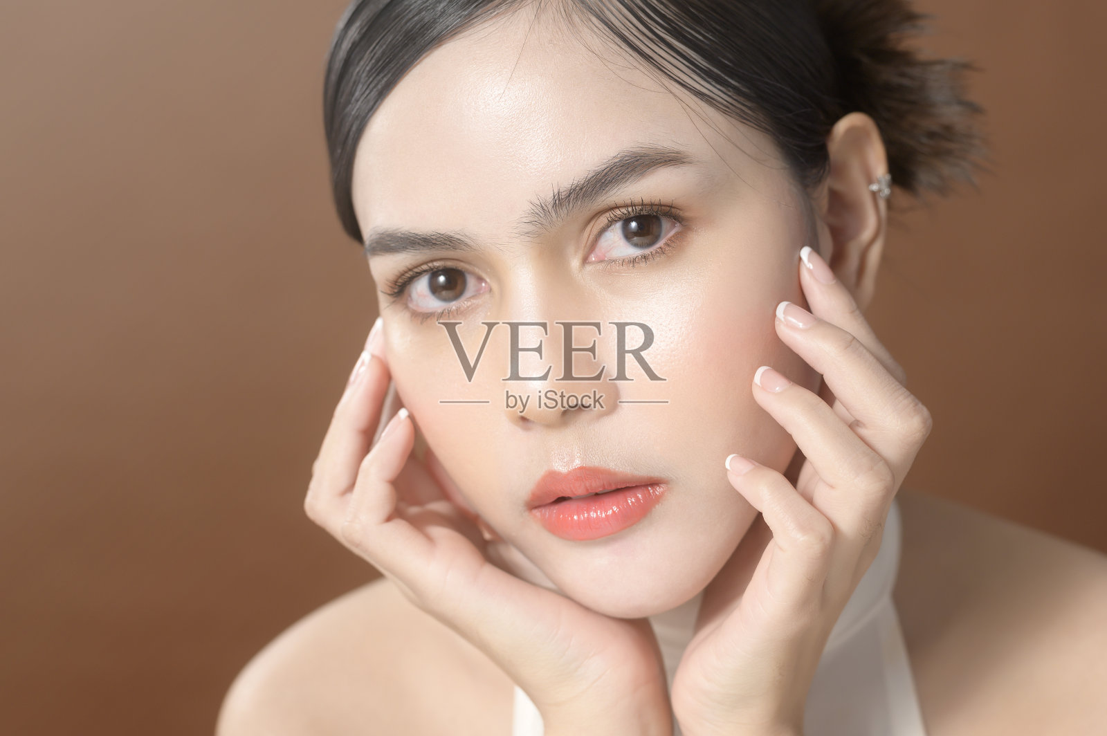 一名年轻女子拥有美丽的面容微笑,触摸她的脸在棕色背景,美容护肤理念照片摄影图片