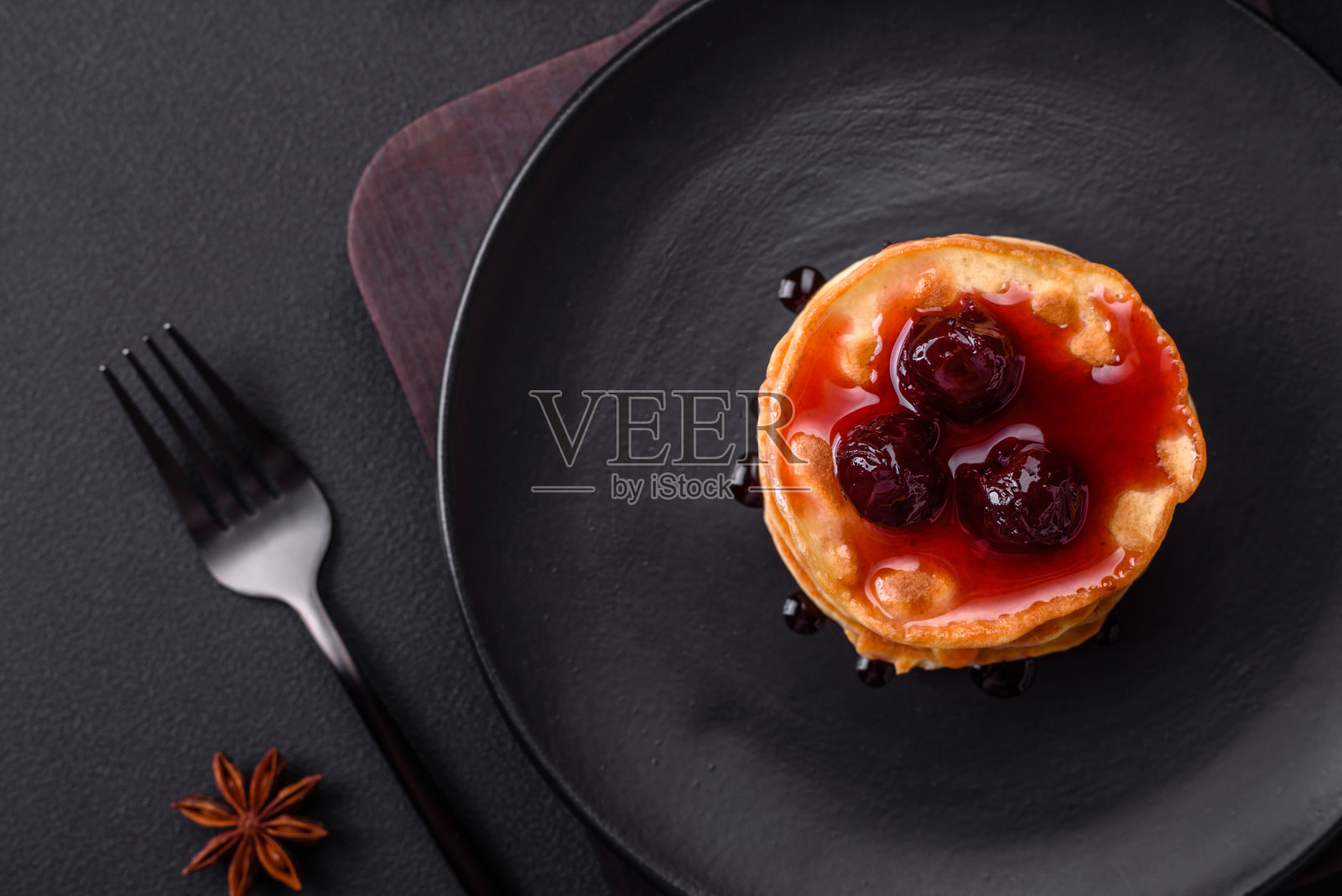 美味新鲜的煎饼和浆果果酱放在黑色的陶瓷盘子里照片摄影图片