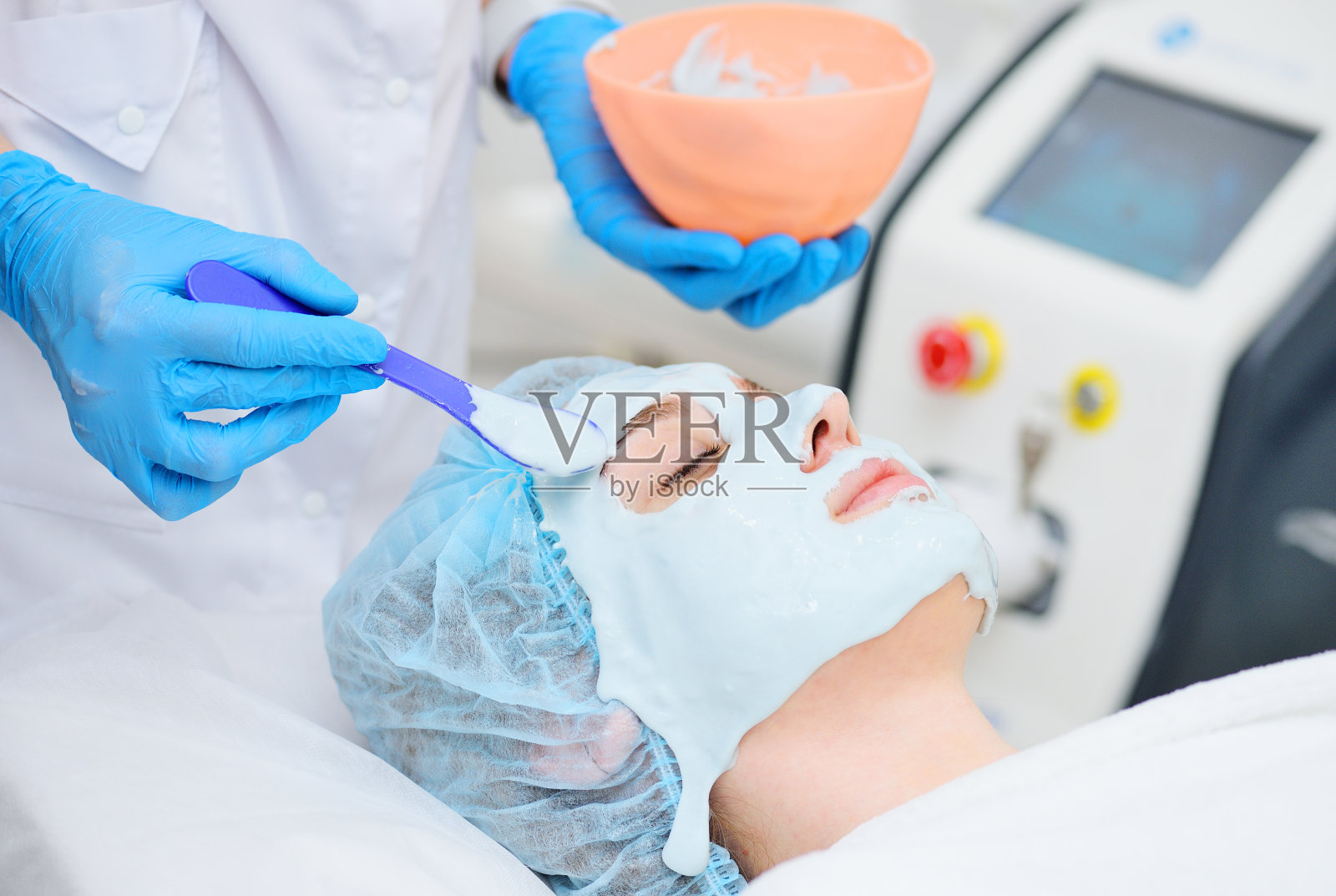 美容师把海藻酸面膜放在一个年轻漂亮的女人的脸上。面部肌肤护理,再生,年轻化照片摄影图片