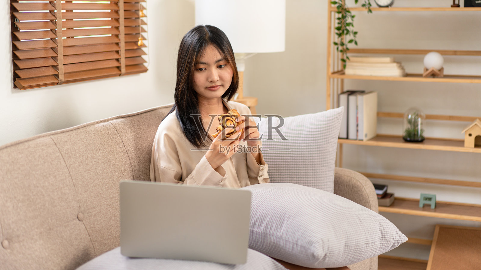 女企业家坐在舒适的大沙发上,一边吃着面包,一边把笔记本电脑放在枕头上照片摄影图片