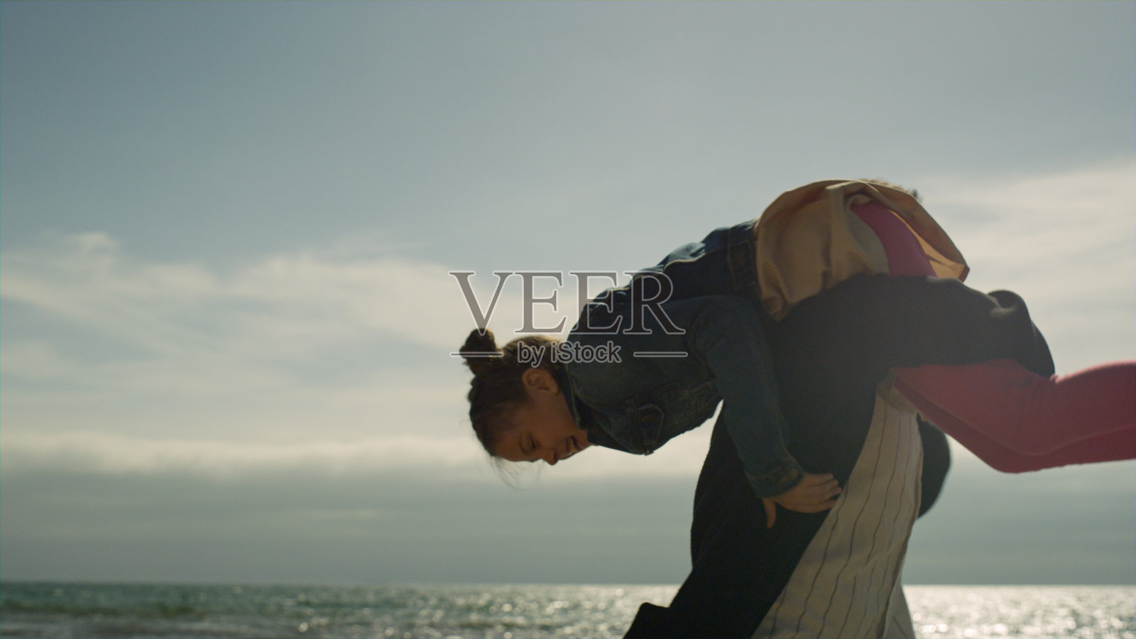 快乐的爸爸在海边抱着孩子。父母和孩子在外面打转。照片摄影图片