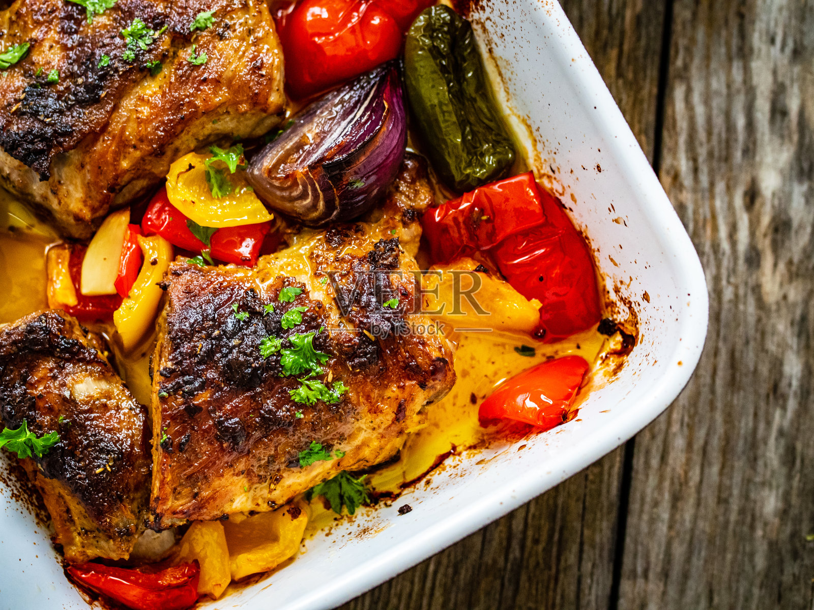 美味的烤排骨配洋葱、彩椒和大蒜,放在木桌上的煎锅里照片摄影图片