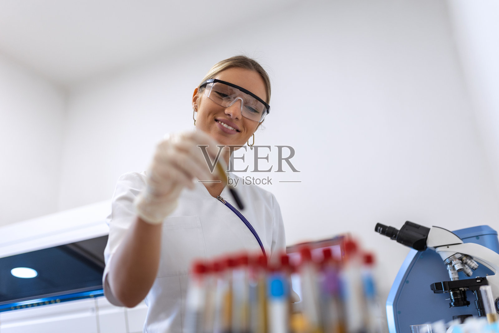 医生从实验室背景的分析机器的架子上取血样管/技术人员在研究实验室拿着血管测试照片摄影图片