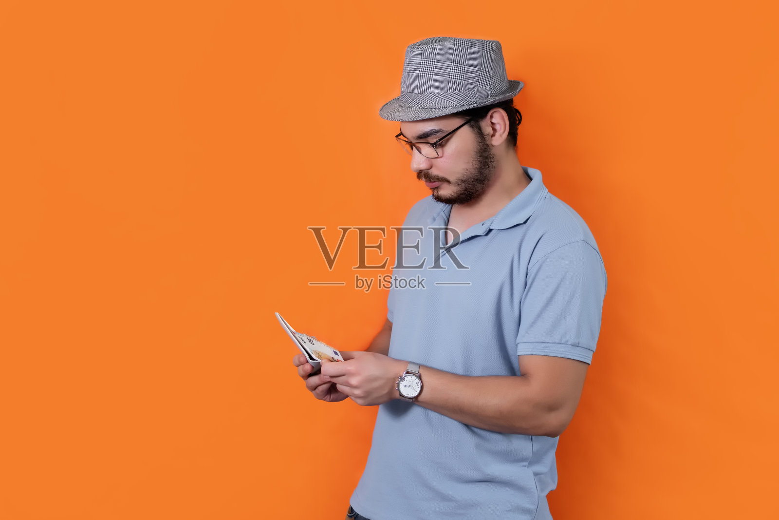 戴着帽子,留着胡子,戴着眼镜的男子在橙色背景中数着欧元照片摄影图片