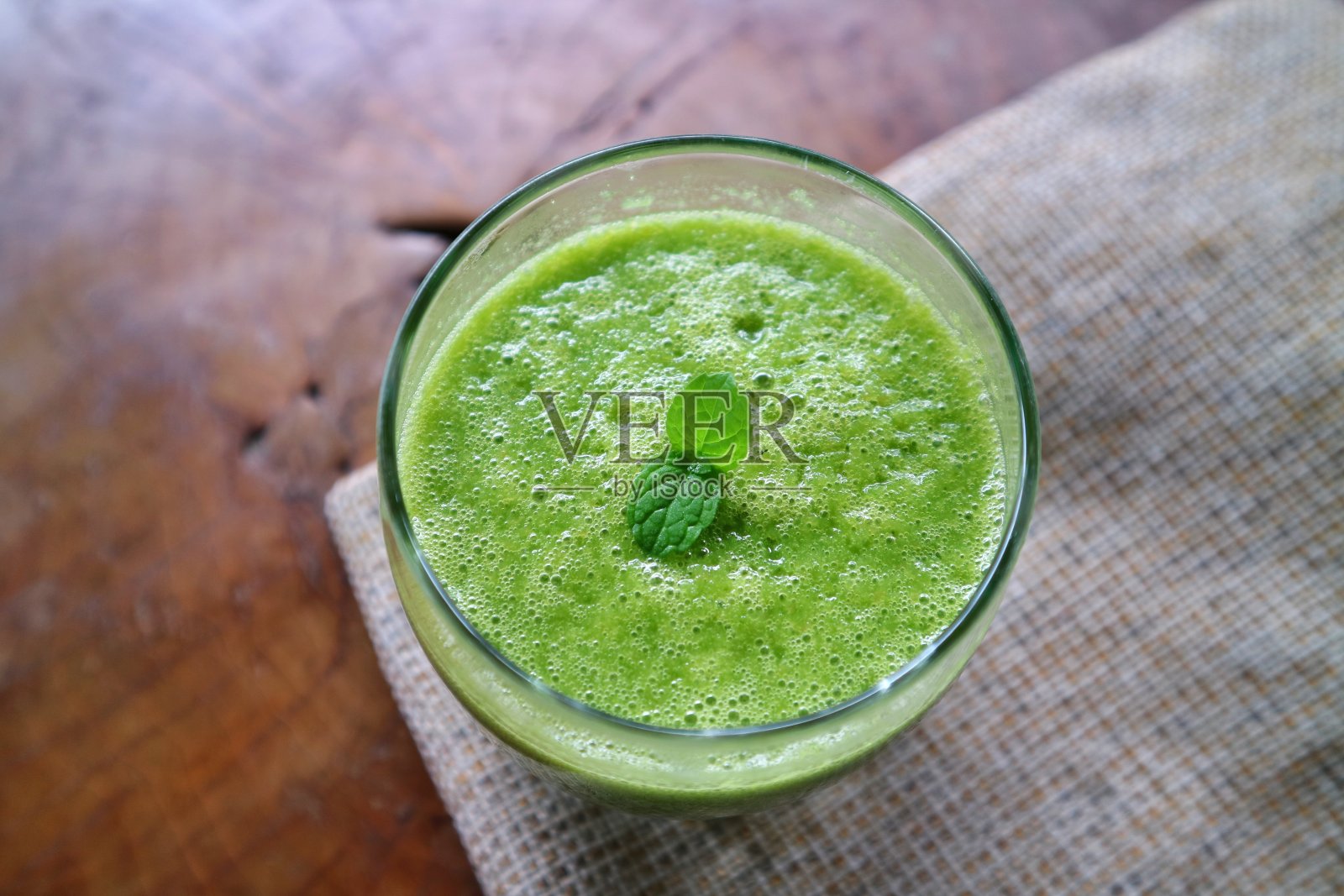 木桌上有一杯绿色的冰沙,上面有薄荷叶。照片摄影图片