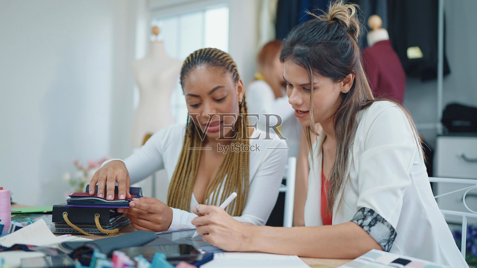 两位专业的亚裔和非裔美国女性时装设计师在服装店讨论设计和选择布料颜色的衣服照片摄影图片