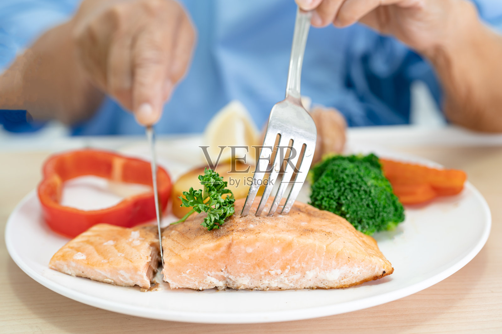 亚洲老年妇女病人在医院饿着肚子坐在床上吃鲑鱼排早餐和蔬菜健康食品。照片摄影图片