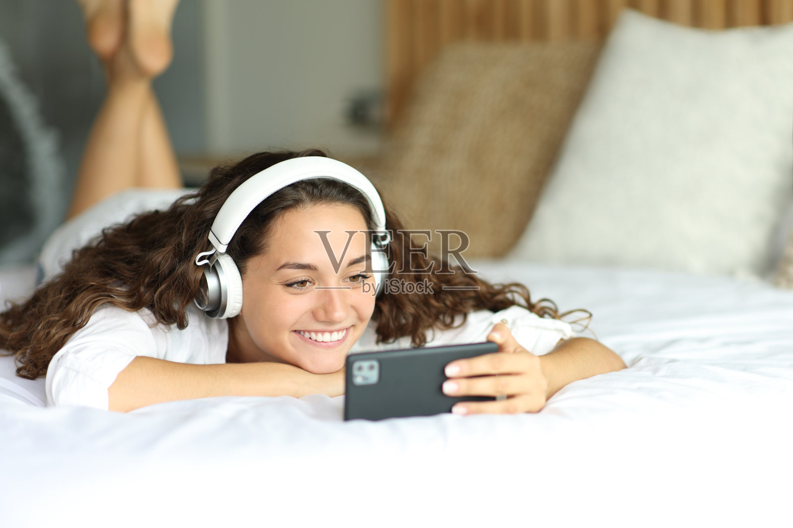 快乐的女人在床上用智能手机看视频照片摄影图片